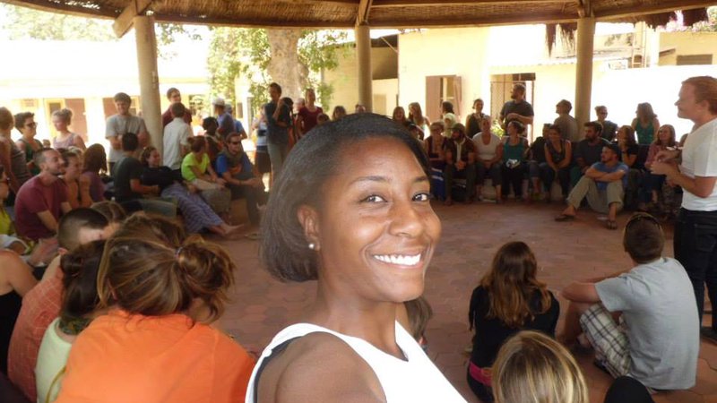 Black Woman Peace Corps Volunteer smiles for the camera with her trainee group sitting in a circle in Senegal.