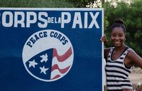 Black woman Peace Corps Volunteer smiles next to Peace Corps sign in French.