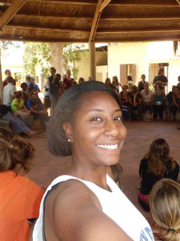 Black Woman Peace Corps Volunteer smiles for the camera with her trainee group sitting in a circle in Senegal.