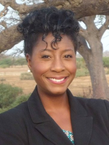 Black Woman Volunteer in formal dress smiles for the camera in Senegal.