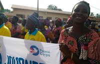 a Beninese woman smiles while marching in a parade with a Peace Corps banner
