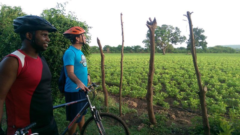 A Latinx Peace Corps Volunteer and a Dominican man stand holding on to mountain bikes. Each is wearing a helmet.