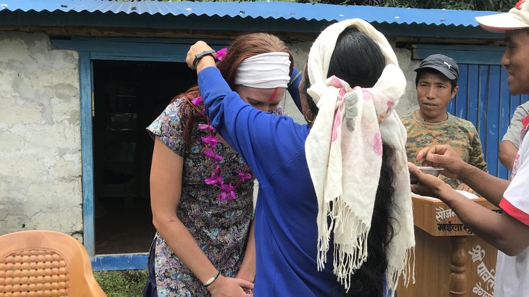 A female Volunteer receives a blessing in the form of a flower necklace from her Nepali host mother.