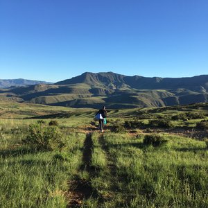 A person walks in the distance through a field in Lesotho. There are mountains in the background and blue skies.