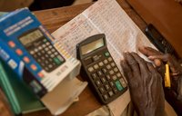 A closeup of a man's hands as works with a calculator and writes numbers in a notebook.