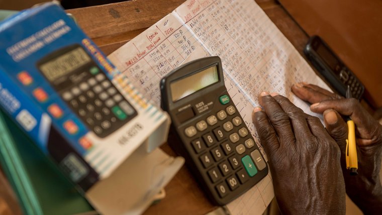 A closeup of a man's hands as works with a calculator and writes numbers in a notebook.