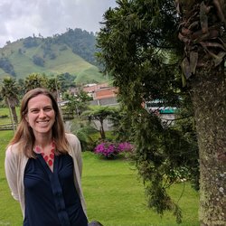 Kait at Decaf Facility in Colombia. She is outside and there are green mountains in the background.
