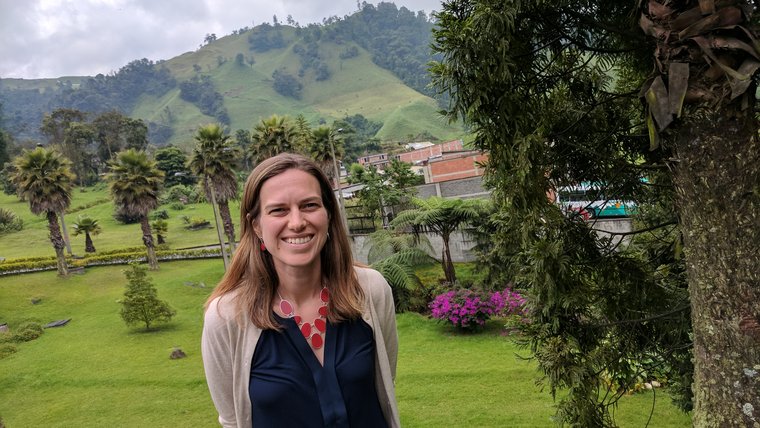 Kait at Decaf Facility in Colombia. She is outside and there are green mountains in the background.