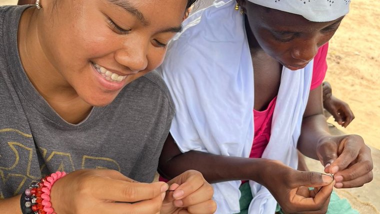 Trinity and a community member create and sell traditional Fula accessories for community fundraising efforts..