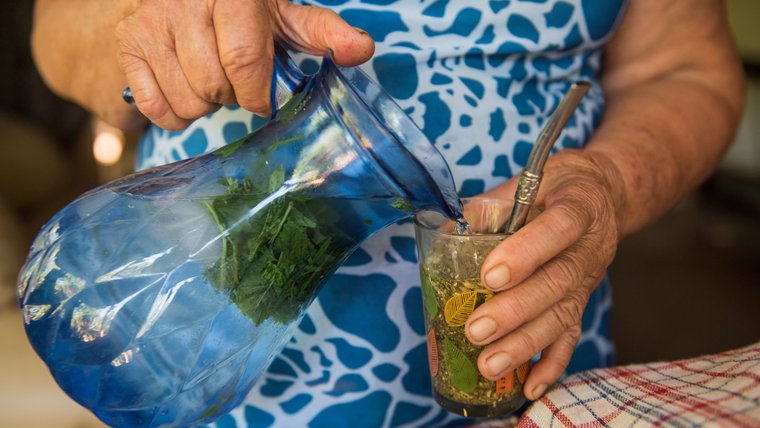 A woman pours terere from a glass pitcher into a glass in Paraguay