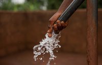The hand of a young girl under running water from a recently built pump.