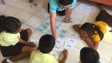 One teacher and four students in a circle looking at cards with words on them