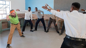 A young white male with a beard stretches with south african students in a circle