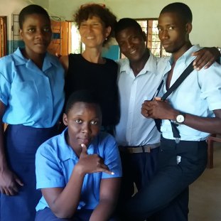 An older Volunteer stands with her Malawian high school students