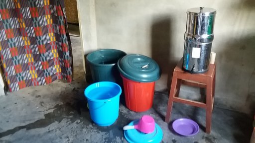 Colorful buckets sit on the floor next to a water filter.