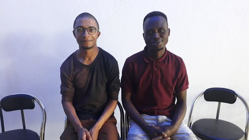 An African American male Peace Corps volunteer and a South African male sit together on folding chairs.