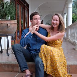 Two Peace Corps Volunteers sit on tiled steps. They are leaning on each other and smiling.