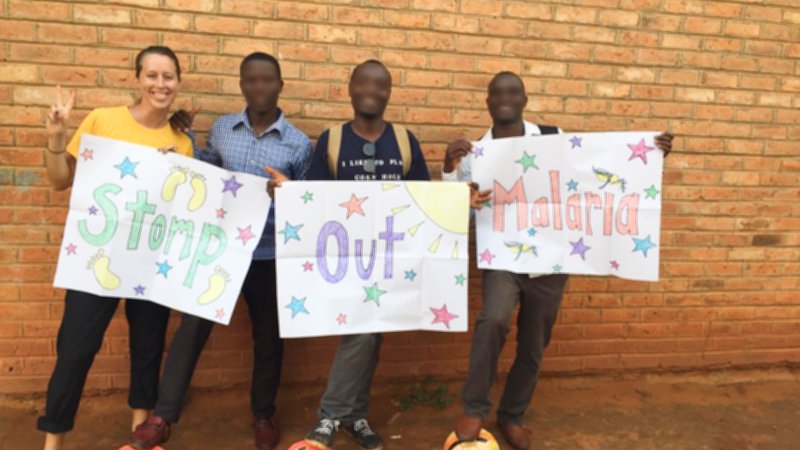 Volunteer and counterparts holding signs that say "Stomp Out Malaria"