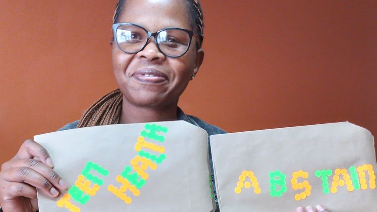 Phindile, teen health officer holds privacy envelopes given to adolescents for completed clinic health questionnaires.