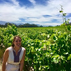 Health Volunteer Anna smiles next to a field of grape vines.