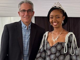 White man with glasses and gray hair stands next to black woman with jewelry and tiara