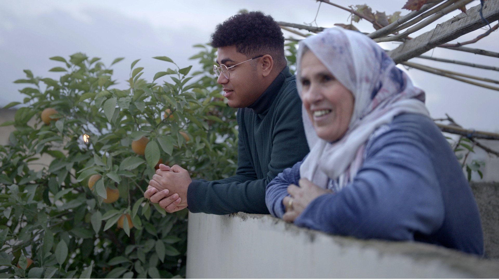 Volunteer and community member talking on a balcony next to an orange tree.