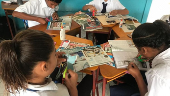 A group of students sit in a circle and cut pictures from magazines