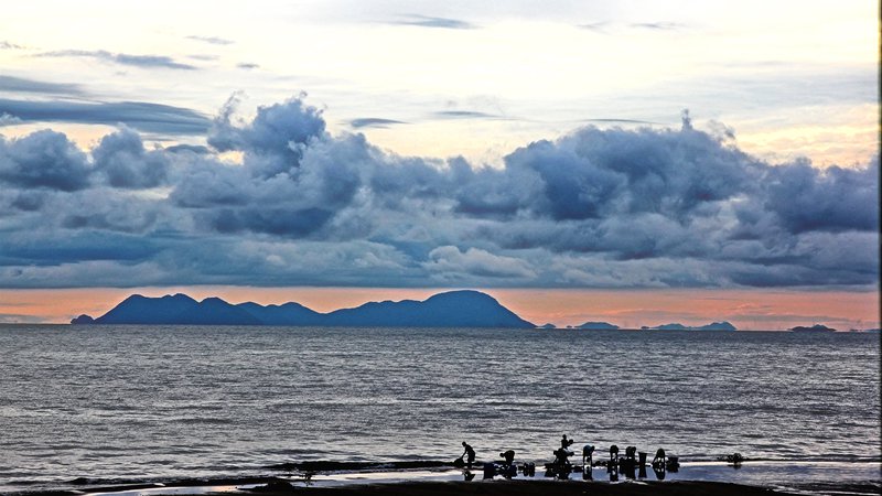 Lake Malawi at morning, with mountains in the background and people washing items in the lake in front.
