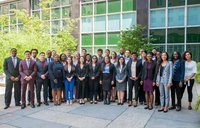 A group of young people in professional clothing stand outside of a building in a large group.