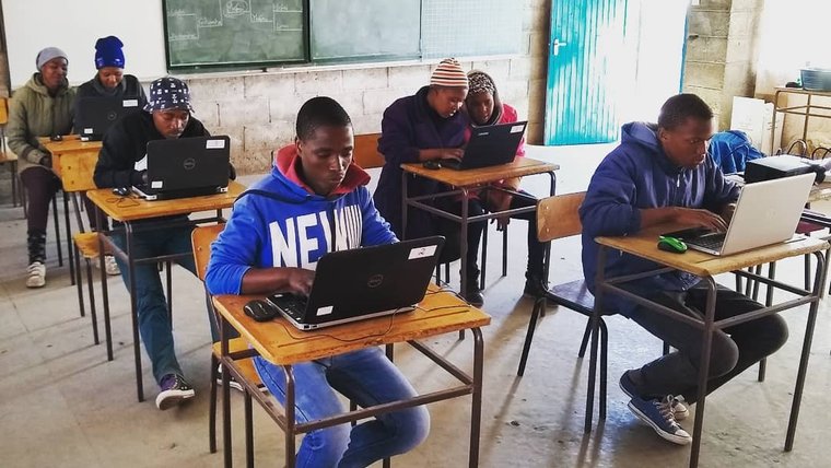 Young African adults it at desks, working on computers, in the computer lab.