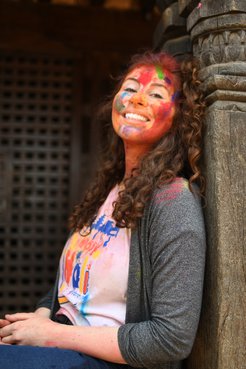 A woman smiles with colorful Holi paint on her face