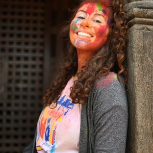 A woman smiles with colorful Holi paint on her face