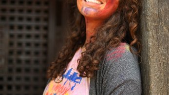A woman smiles with colorful Holi paint on her face