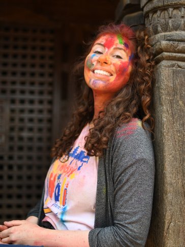 A woman smiles with colorful Holi paint on her face
