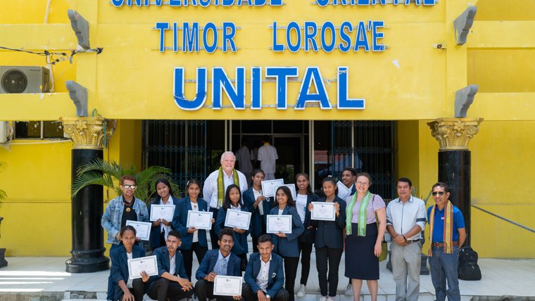 Teachers in training stand in front of their university with certificates