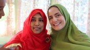 Two women pose for a photo wearing hijab. One is in a red hijab, the other in green.