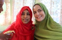 Two women pose for a photo wearing hijab. One is in a red hijab, the other in green.