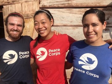 Three people-one man and two women-smiling and posing together, all wearing shirts featuring the Peace Corps logo