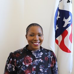 Staff member stands in front of Peace Corps flag