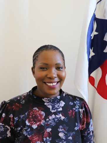 Staff member stands in front of Peace Corps flag