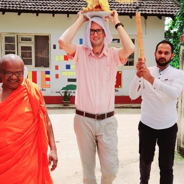 Male PCV carrying casket with relics at village religious event under a decorated umbrella with Buddhist priest and another man