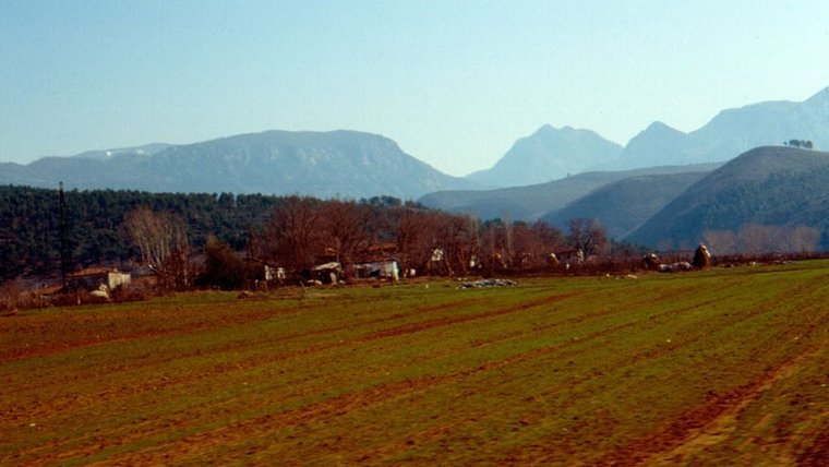 An aged, scenic photo of farmland with distant mountains