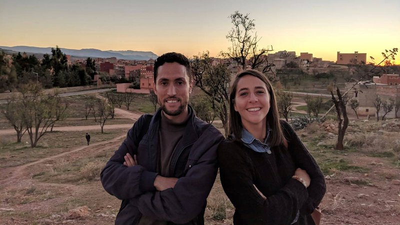Alena and her counterpart pose back to back. Behind them the sun sets on a small Moroccan town.