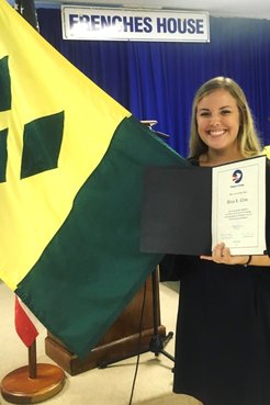 A blonde woman holds a certificate and flag