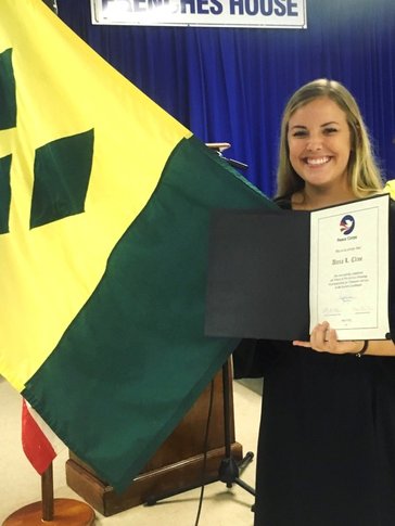 A blonde woman holds a certificate and flag