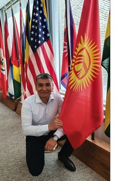 One man kneels on one knee beside the Kyrgyz Republic flag