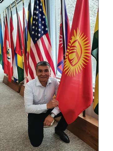 One man kneels on one knee beside the Kyrgyz Republic flag