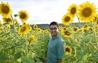An individual with glasses stands in a field of sunflowers.