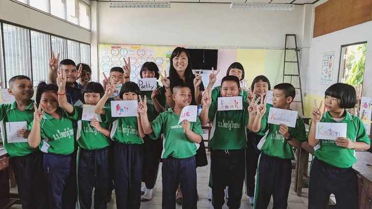 Volunteer Andrea poses with a class of primary school kids. They all hold up homemade name tags and peace signs.