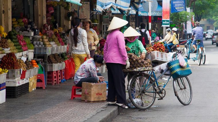 Shoppers load fruit onto a bicycle at an open-air market.